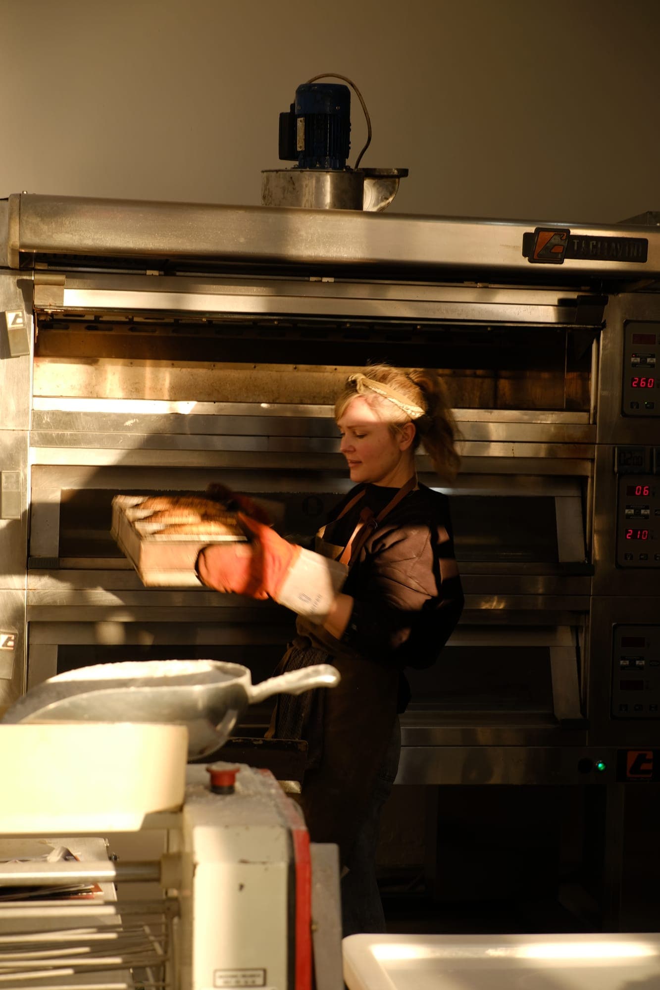 Alva pulling a fresh tray of bread from the deck oven at dawn